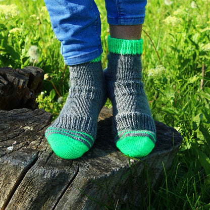 Hand-knitted acrylic socks with green accents perched on an old tree stump